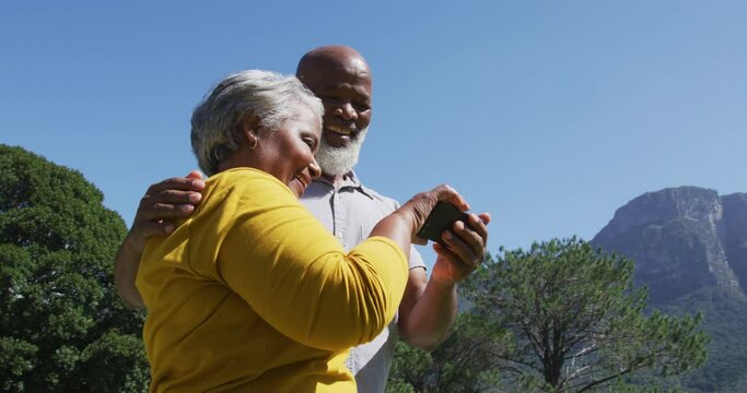 Happy senior african american couple using smartphone taking selfie in sunny garden