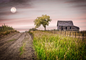 beautiful moon shining in an early evening sunset over an old wood abandoned house.