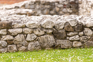 Remnants of old buildings. Archaeological ruins preserved for tourists. White stones and green grass with white flowers.