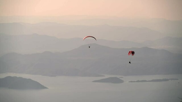 Paragliders flying with paragliding in sky over the forest, mountain top and sea.Parachute atmosphere drag parachutes parasailing parascending parakiting parasail fly flight aerial air sport tandem 4K