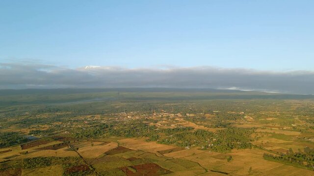 Aerial view of a town and sunlit fields, golden hour in rural Africa - tracking, drone shot