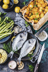 Fresh uncooked dorado or sea bream fish with lemon ,asparagus, herbs, olive oil and spices over...