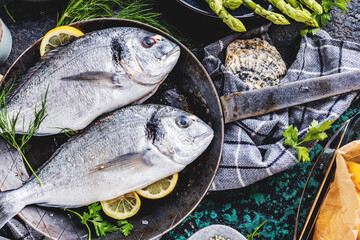 Fresh uncooked dorado or sea bream fish with lemon ,asparagus, herbs, olive oil and spices over...