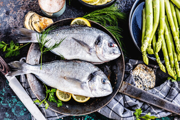 Fresh uncooked dorado or sea bream fish with lemon ,asparagus, herbs, olive oil and spices over...