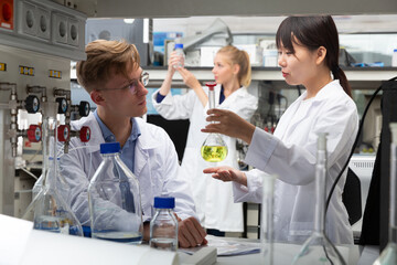 Fototapeta premium Young Caucasian and Asian students engaged in research at chemical lab