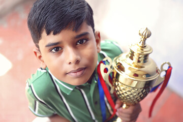 Indian school boy holding a golden trophy cup	