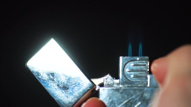 Silver Zippo lighter ignites in front of black background. Lighter close up. Slow motion.