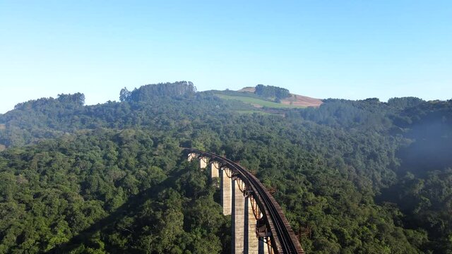 Aerial view of high railroad bridge track accross a valley into a hill with native forest under the morning mist
