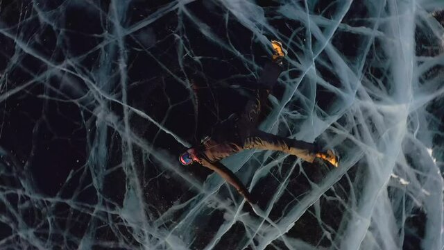 A man lies on the ice in winter, swinging his arms and legs to the side, pretending that he is swimming in the water. Approaching drone aerial view of the frozen lake Baikal.