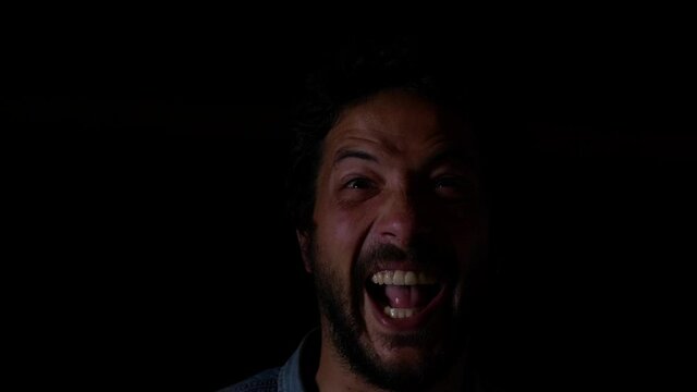 Insane man emerging from black background facial expression crazy laughing hysterically