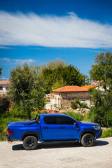 Fototapeta premium Side, Turkey – April 15 2021: blue Toyota Hilux parked on the street on a warm summer day against the backdrop of old street, trees, palms