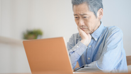 ノートパソコンの前で困惑するシニア男性