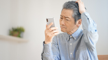 スマートフォンの操作に悪戦苦闘するシニア男性