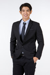 Portrait shot of Asian young black short hair smart confident businessman entrepreneur in formal suit with necktie standing smiling hold hands in pockets look at camera in front of white background