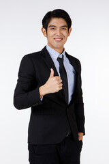 Portrait shot of Asian young happy confident white collar businessman in black stylish modern formal suit standing smiling look at camera showing thumb up admiring in front of white background
