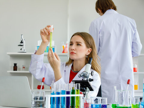 Woman caucasian are scientist look at sample in tes tube and scientist man standing at back in laboratory.