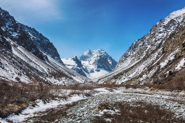 Idyllic winter landscape with hiking trail in the mountains. Rocks, snow and stones in mountain valley view. Mountain panorama.
