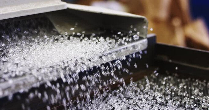 Beads from glass falling to conveyor belt in factory, slider extreme closeup view