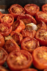 Halves of sun-dried tomatoes with spices and garlic. Natural background with tomato slices. Image with selective focus.