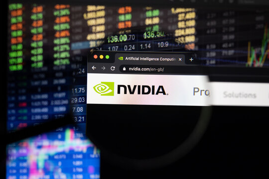 Nvidia company logo on a website with blurry stock market developments in the background, seen on a computer screen through a magnifying glass