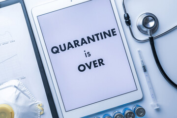 End of quarantine. Medical equipment: doctor stethoscope, hospital healthcare charts, syringe with needle and white tablet with text on screen. Quarantine is over concept.