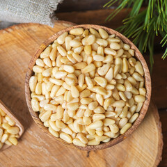 Round bowl with peeled pine nuts, on the background of a round wooden board. View from above.