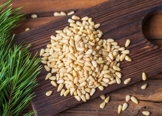Peeled pine nuts are heaped on a dark wooden cutting board. View from above.