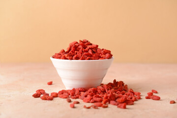 Bowl with dried goji berries on color background