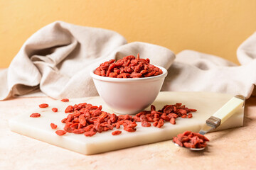 Bowl with dried goji berries on color background