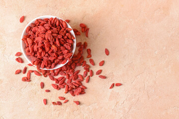 Bowl with dried goji berries on color background