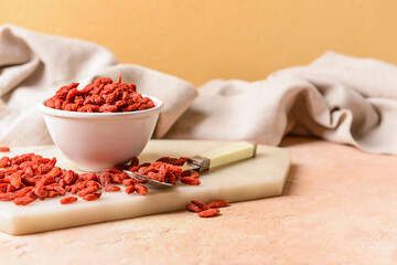 Bowl with dried goji berries on color background