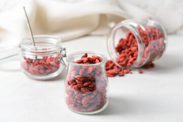 Jars with dried goji berries on light background