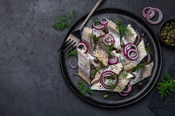 Obraz na płótnie Canvas pickled herring with red onion, capers and dill on black plate