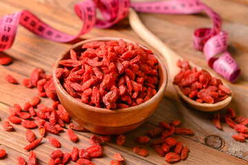 Measuring tape, spoon and bowl with dried goji berries on wooden background