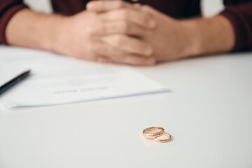 Man with divorce decree and rings in lawyer's office, closeup - obrazy, fototapety, plakaty