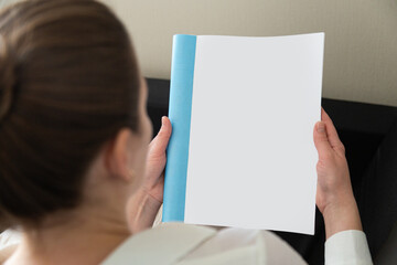 Beautiful female hands hold an open book or magazine in a room on a black sofa