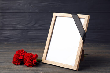 Blank photo frame with carnation flowers on dark wooden background