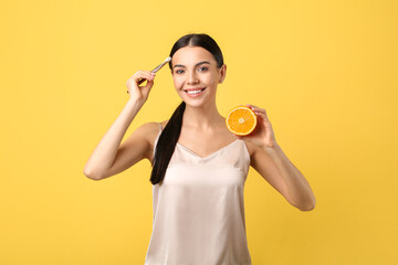 Beautiful woman with orange applying facial cream on color background