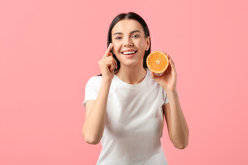 Beautiful woman with orange applying facial cream on color background