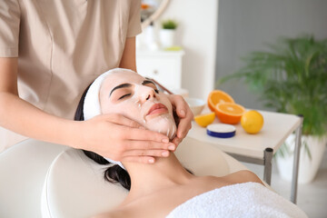 Obraz na płótnie Canvas Cosmetologist applying sheet mask on woman's face in beauty salon