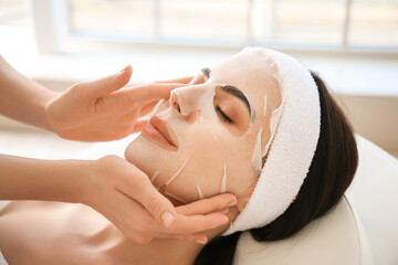 Cosmetologist applying sheet mask on woman's face in beauty salon