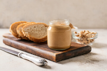 Jar with tasty peanut butter and pieces of bread on light background