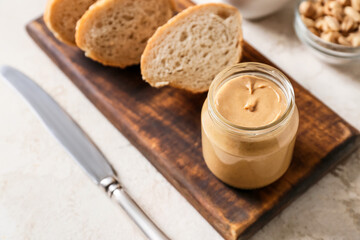 Jar with tasty peanut butter and pieces of bread on light background