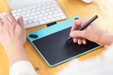 Close-up of female hands using digital graphics tablet and stylus while working in modern office