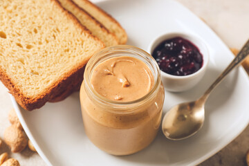 Jar with tasty peanut butter, toasts and jam on light background, closeup
