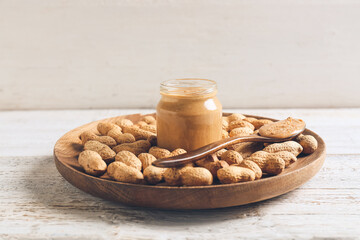 Jar and spoon with tasty peanut butter on light wooden background