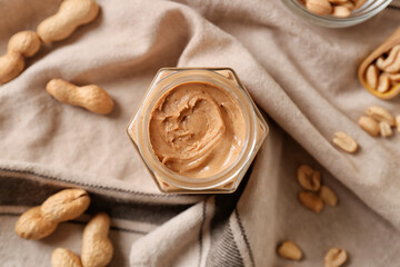 Jar with tasty peanut butter on fabric background