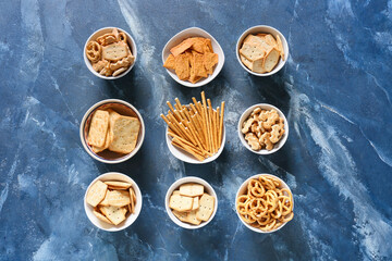 Bowls with tasty different crackers on color background