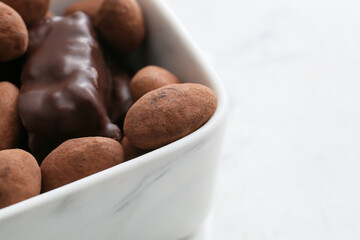 Bowl with tasty chocolate candies on light background, closeup