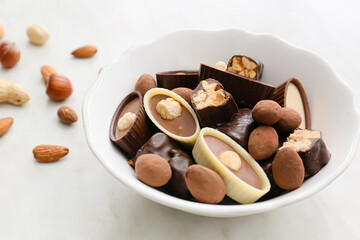 Bowl with tasty chocolate candies on light background, closeup